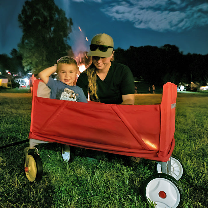 Child sitting in wagon at night being watched by his mom while a bonfire blazes in background