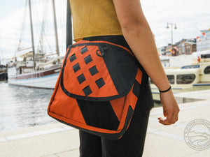 Orange Transit Bag being carried by a young woman who is traveling the world, near the edge of a dock with sail boats