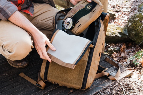 Person opening a coyote brown backpack outdoors with a natural setting