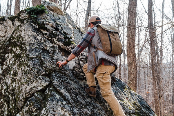 Person with a backpack climbing a rocky outcrop in a forest