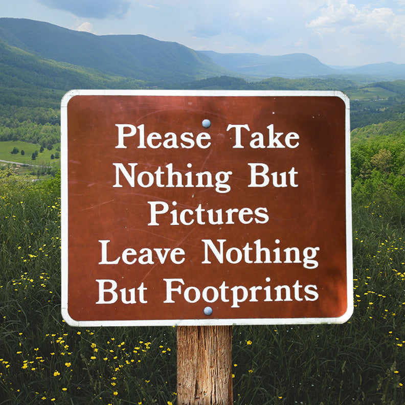 'Please take nothing but pictures, leave nothing but footprints' sign in field with mountains in distance