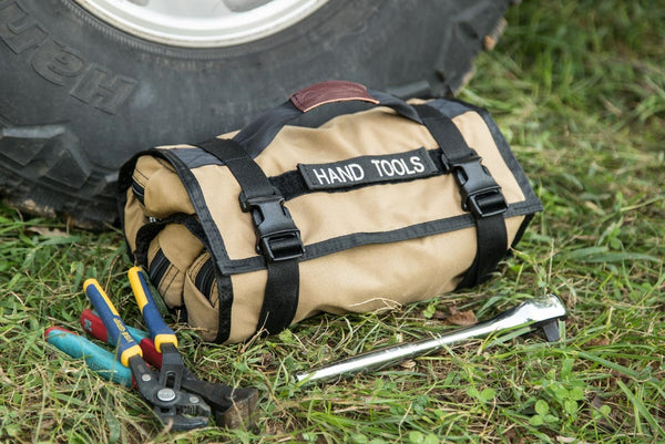 Coyote BROG Tool Pouch Roll labeled “Hand Tools” beside an off-road tire, with pliers and a ratchet laid out on the grass.