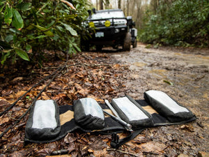 BROG Tool Pouch Roll opened on a muddy off-road trail with four removable tool pouches and hand tools, with an overland vehicle in the background.